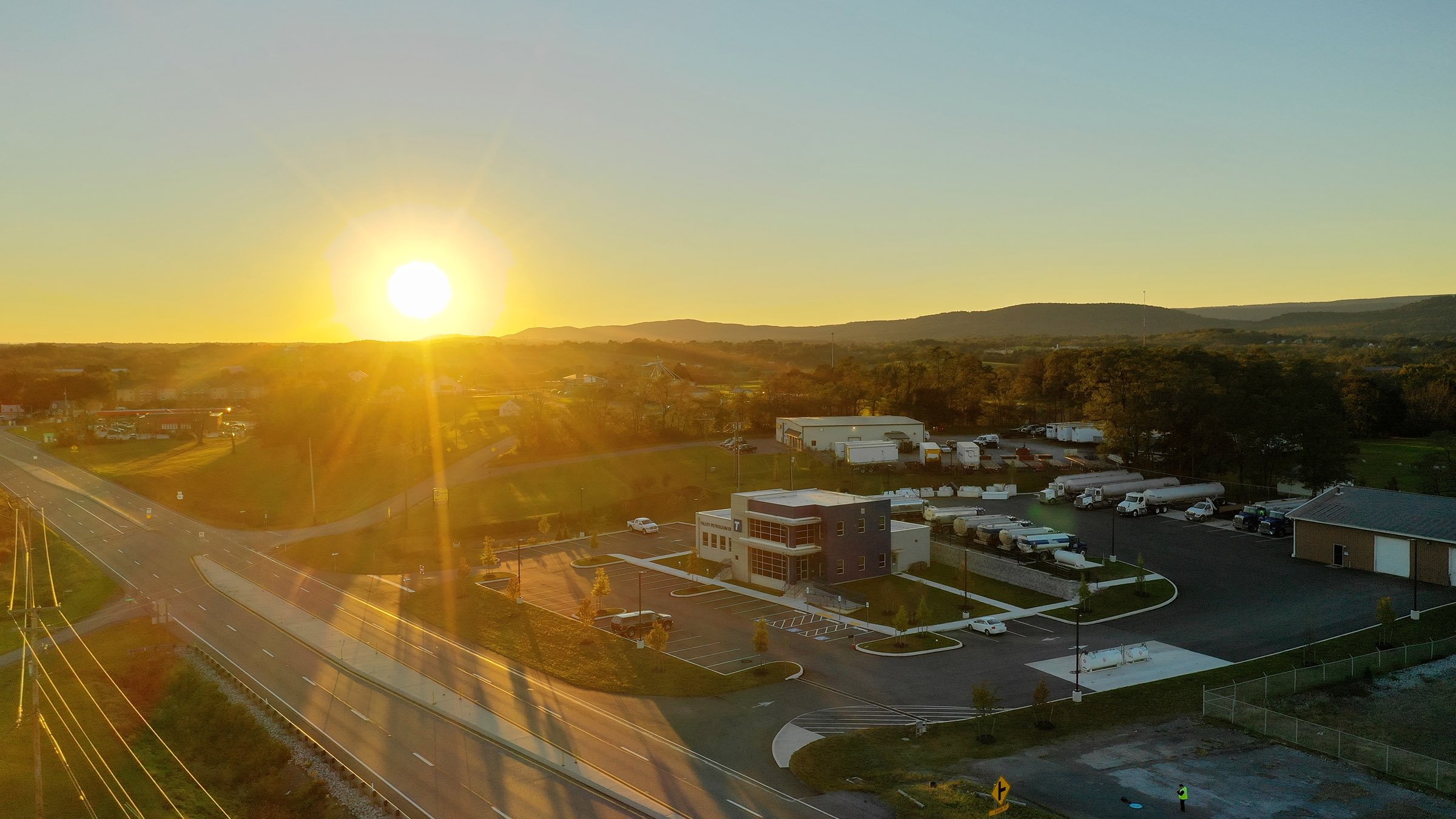 Aerial view of a commercial petroleum company building and fuel trucks at golden hour